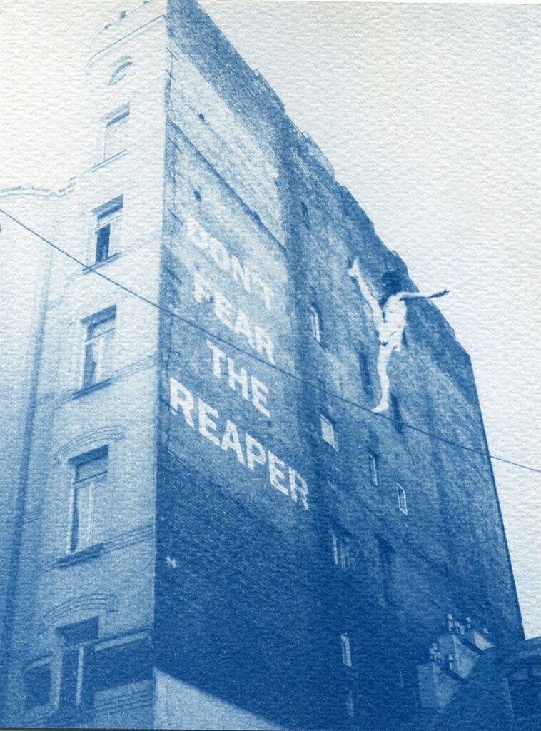 Vieil immeuble varsovien photographié en contre-plongée avec l'ajout par collage de l'inscription "Don't fear the reaper" sur la façade ainsi que d'une funambule sur le fil électrique qui barre la photo.