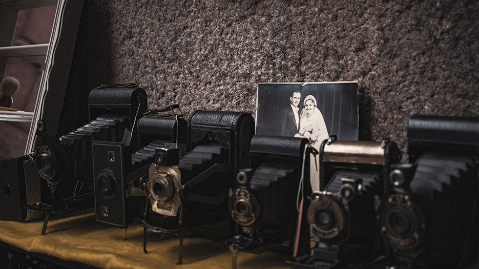 Une série de très vieux appareils photo à soufflet avec le cliché ancien d'un couple jeune marié posé à côté.