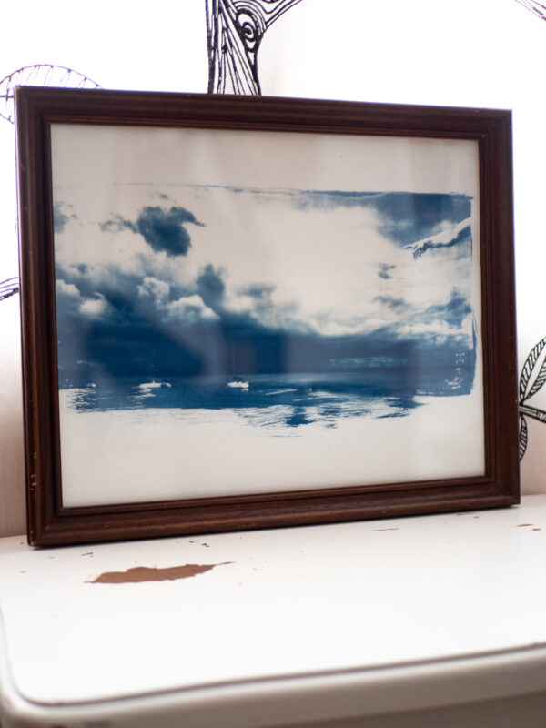 Cyanotype dans son cadre ancien en bois foncé. La photo représente un orage en formation dans la baie de Guérande. On distingue quelques bateaux de plaisance, des nuages très contrastés et l'ajout par collage du bras de Dieu dans La Création d'Adam de Michel-Ange.