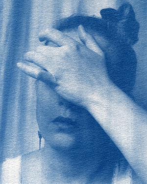 Autoportrait cyanotype. Plan serré sur la tête, la main posée sur les yeux.